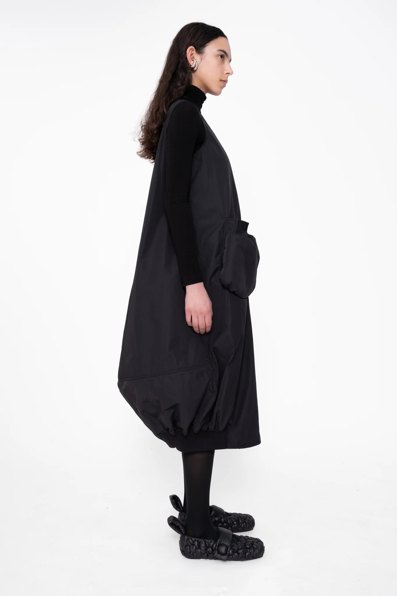female-wearing-black-bomber-dress-with-big-front-pocket-on-white-background-full-body-side