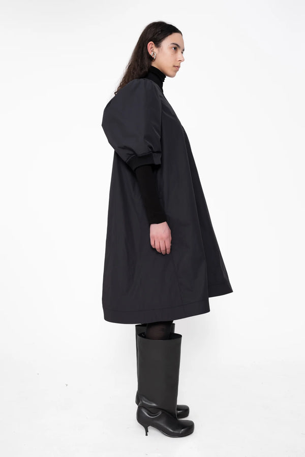 female-wearing-black-bomber-dress-with-zip-and-puffed-cropped-sleeves-and-double-heel-boots-on-white-background-full-body-side