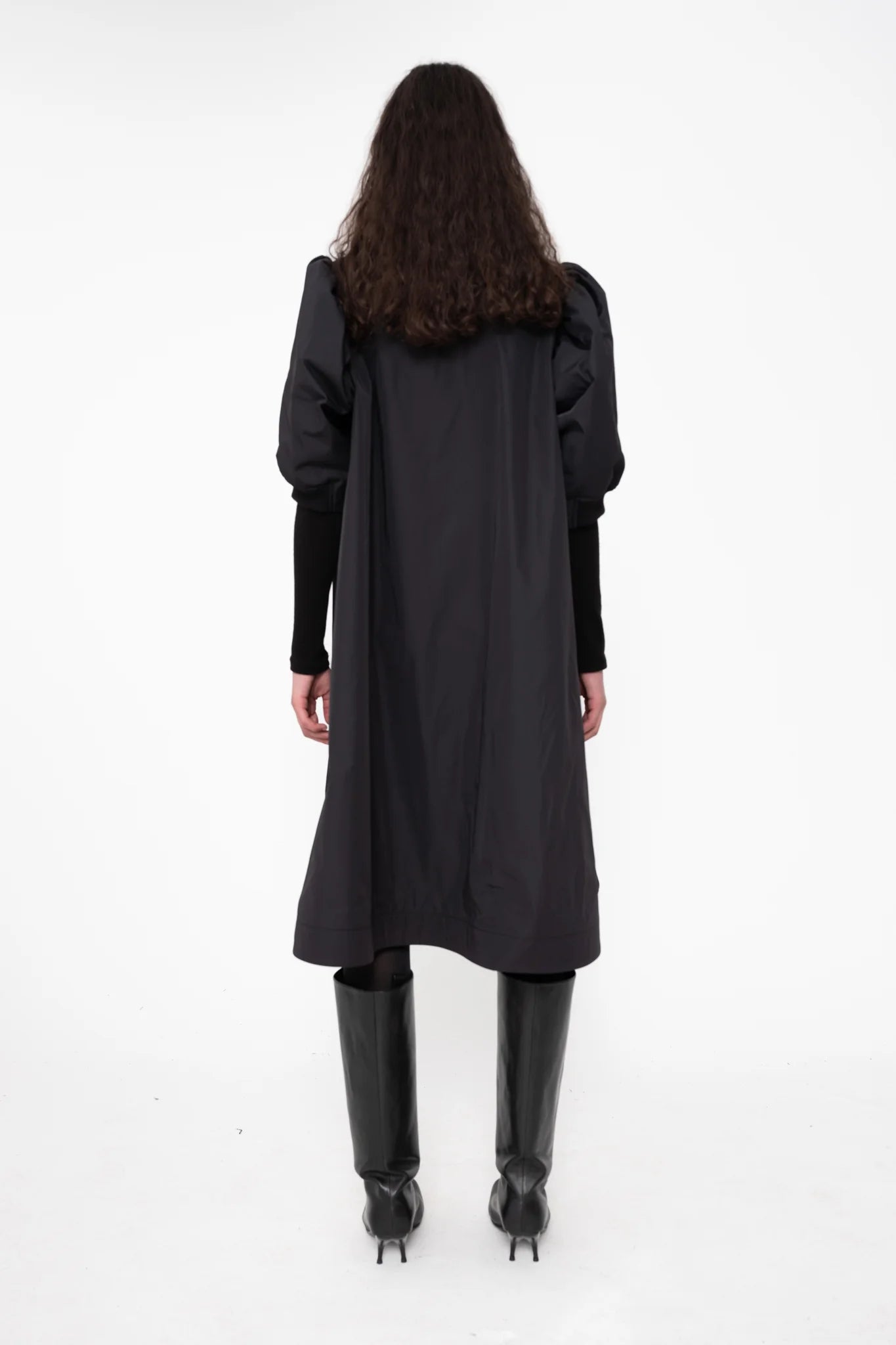 female-wearing-black-bomber-dress-with-zip-and-puffed-cropped-sleeves-and-double-heel-boots-on-white-background-full-body-back