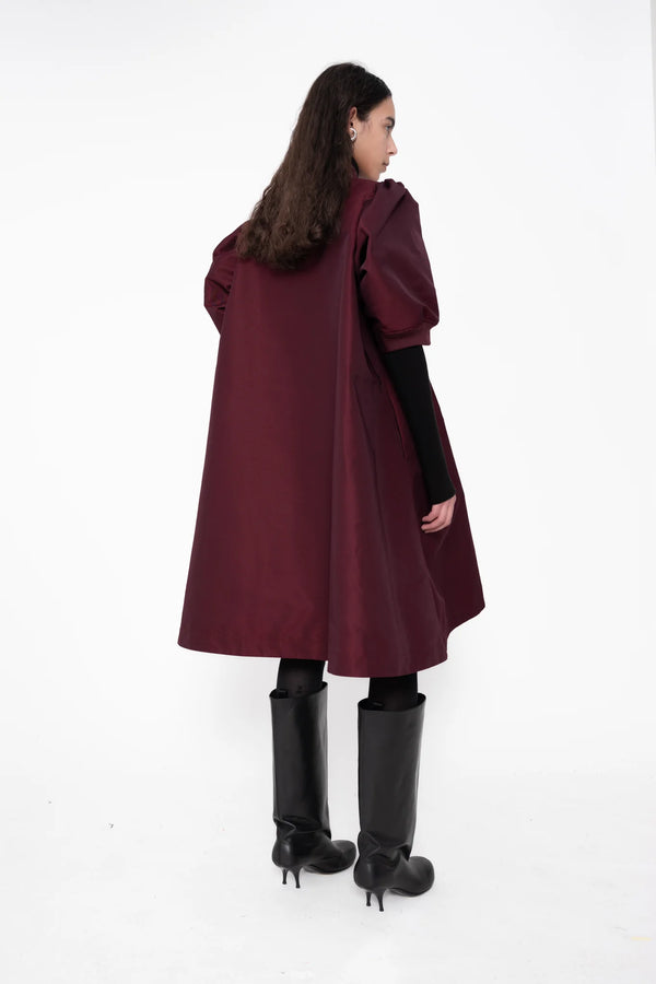 female-wearing-bordeaux-midi-bomber-dress-with-zip-and-cropped-puffed-sleeves-with-black-underlayer-and-boots-on-white-background-full-body-back-side