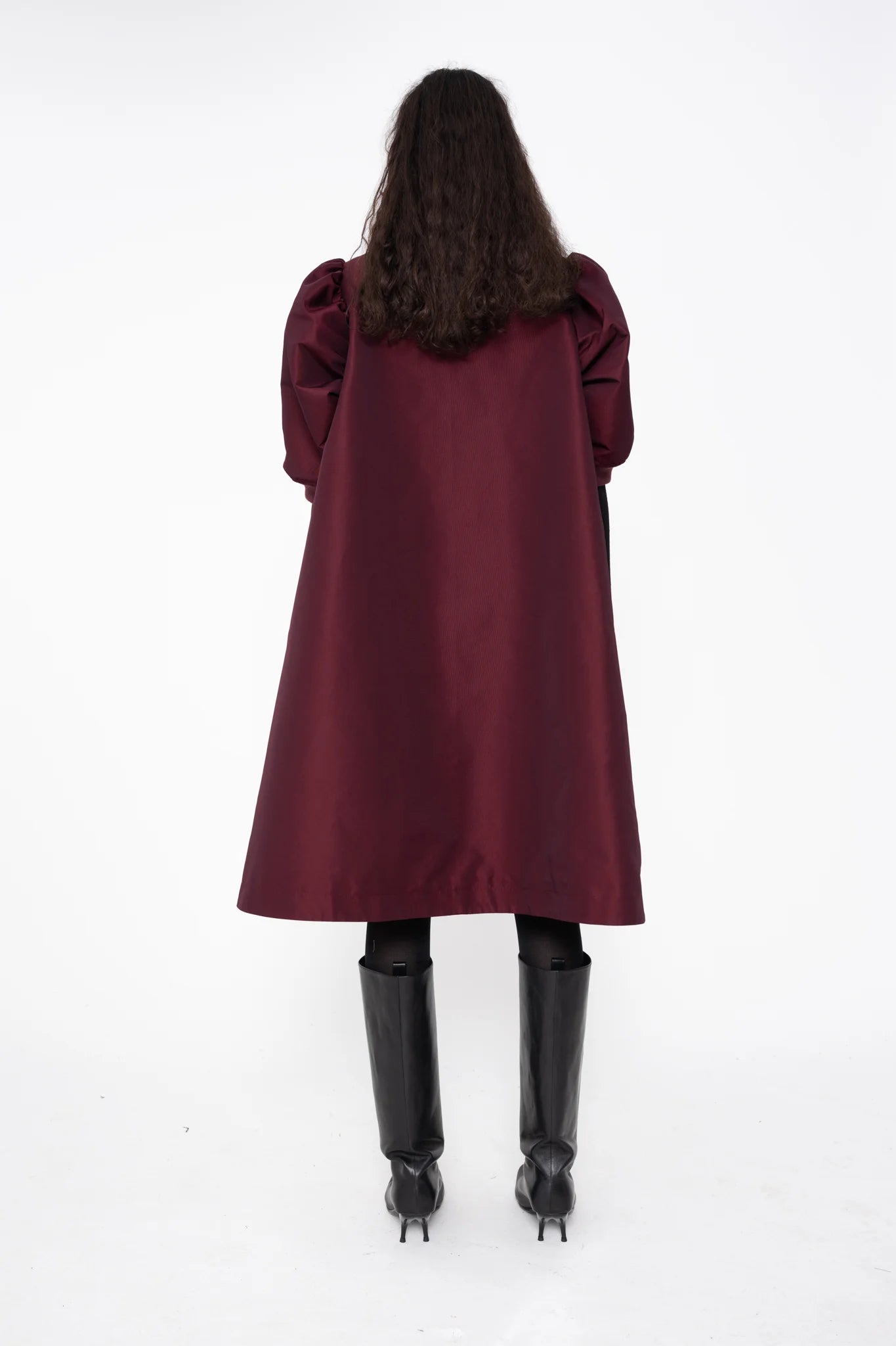 female-wearing-bordeaux-midi-bomber-dress-with-zip-and-cropped-puffed-sleeves-with-black-underlayer-and-boots-on-white-background-full-body-back