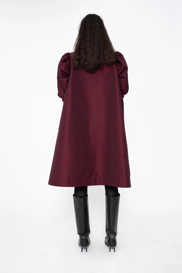 female-wearing-bordeaux-midi-bomber-dress-with-zip-and-cropped-puffed-sleeves-with-black-underlayer-and-boots-on-white-background-full-body-back
