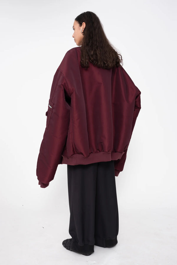 female-wearing-oversized-bordeaux-bomber-jacket-with-slits-at-armholes-and-black-underlayer-top-with-black-suit-pants-on-white-background-full-body-one-quarter