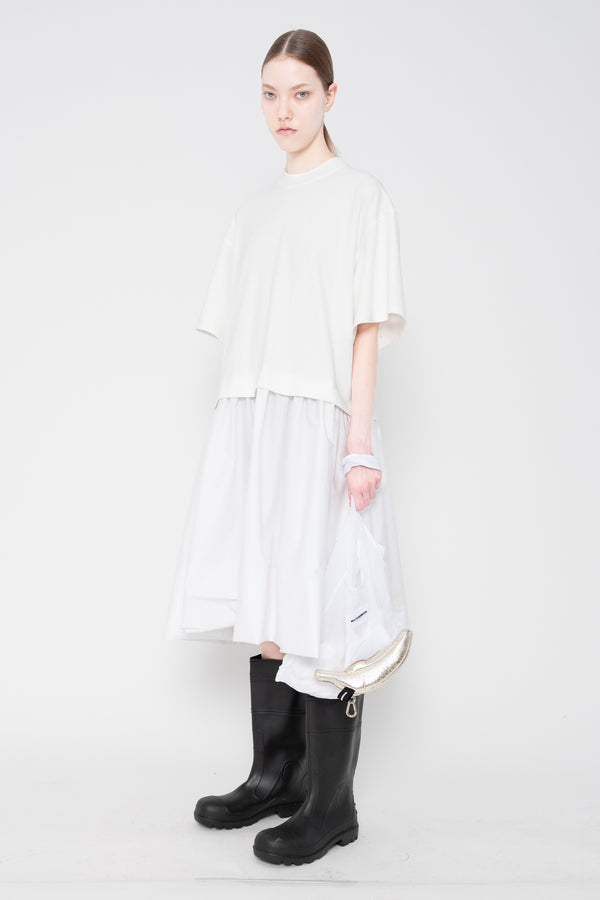 Person wearing a white dress and black rain boots on a plain background