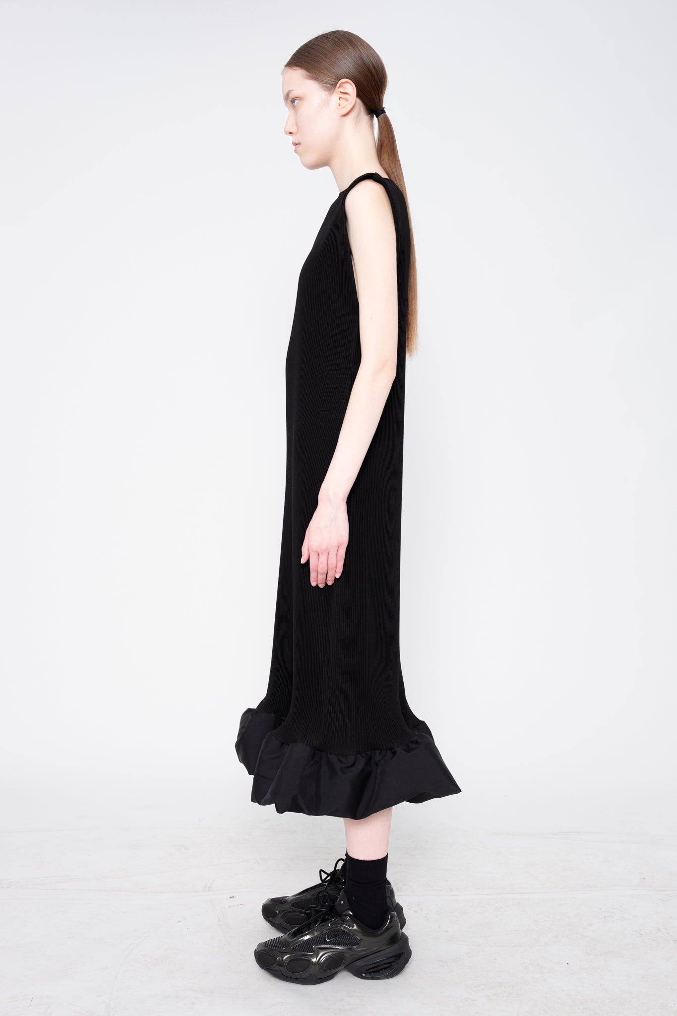 Woman wearing a black sleeveless dress with ruffled hem on a white background