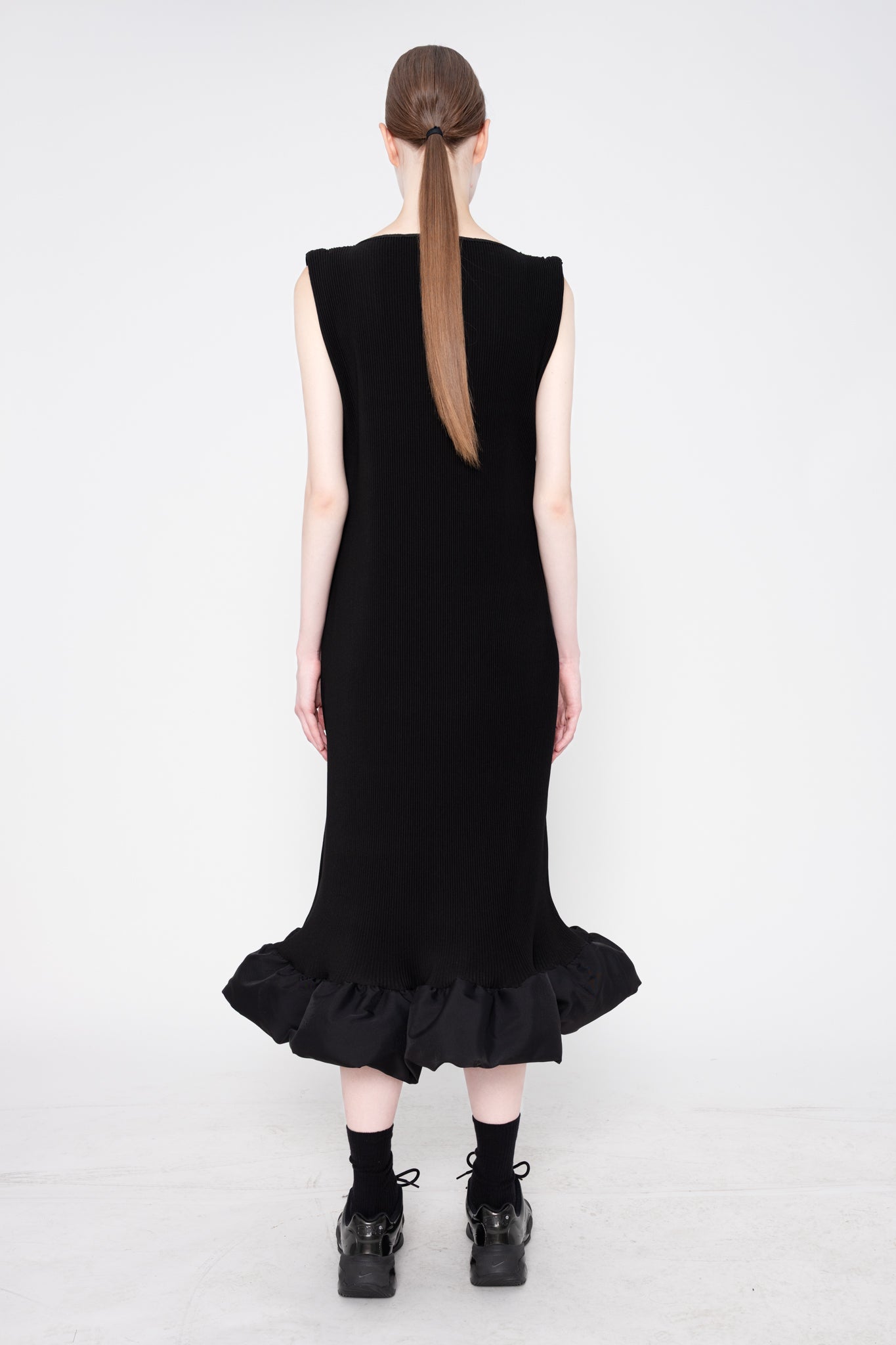 Person wearing a black dress with ruffled hem on a white background