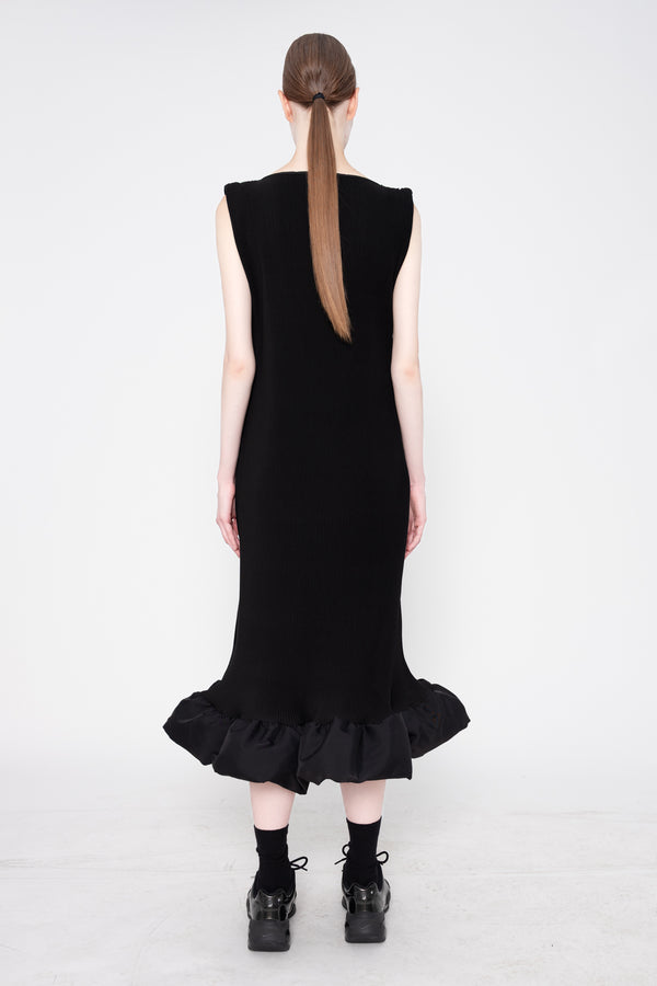 Person wearing a black dress with ruffled hem on a white background