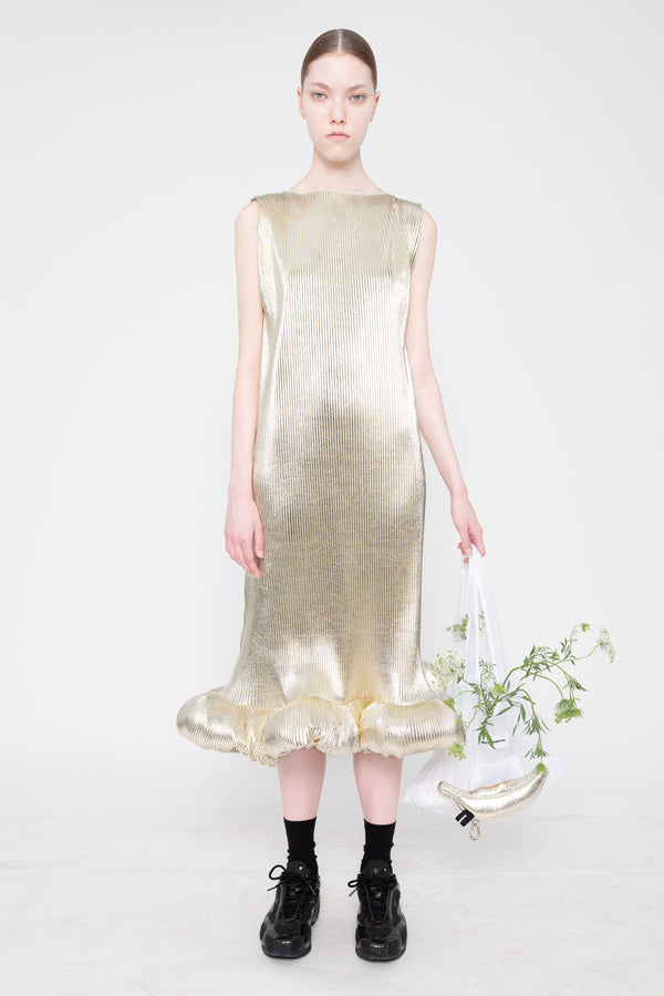 Model wearing a gold dress holding a white bag with greenery on a white background