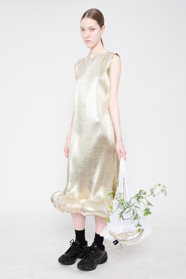 Woman wearing a gold dress holding a white bag with greenery on a white background