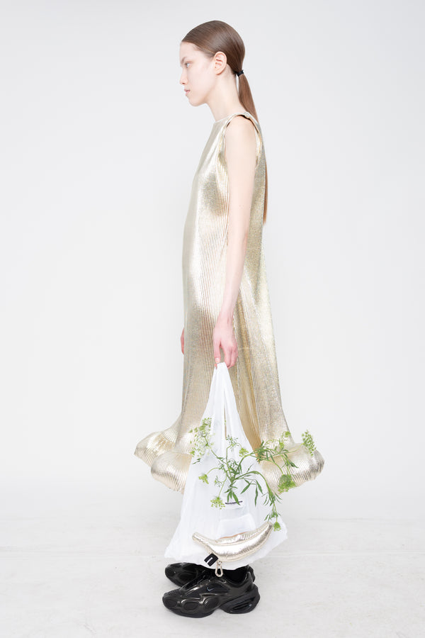 Woman wearing a long, light-colored dress with a floral bag on a white background
