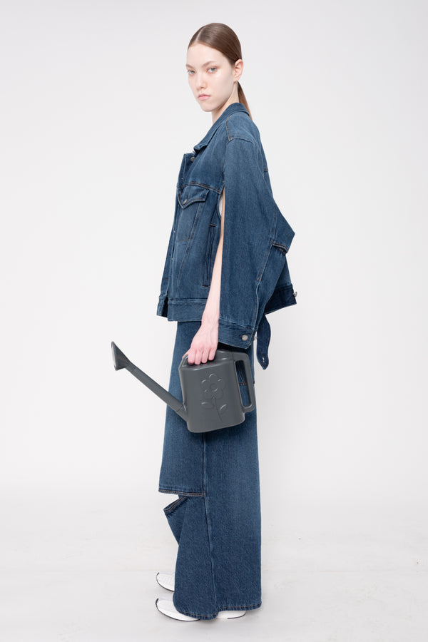 Person wearing a blue denim outfit holding a black bag on a white background