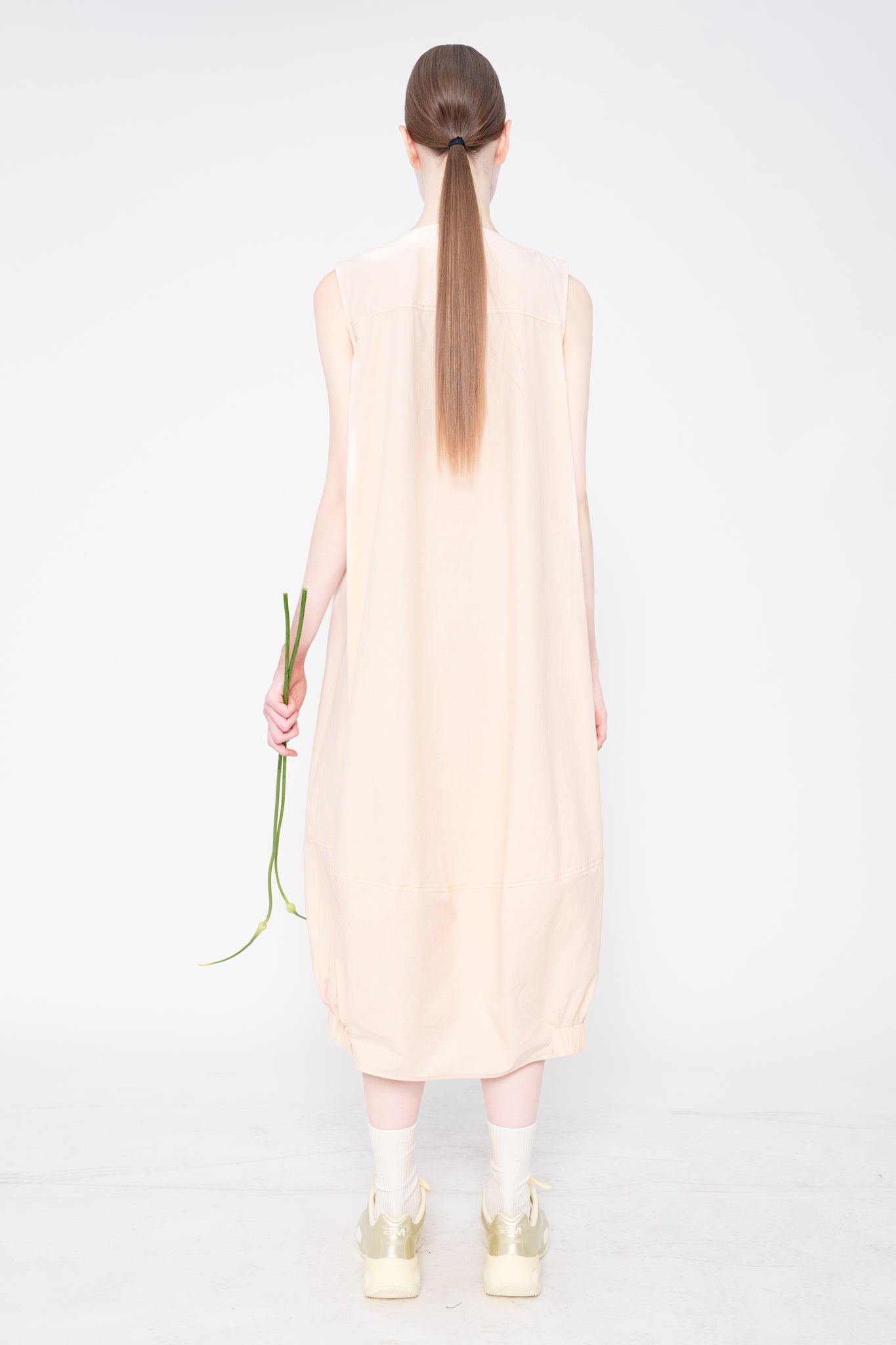 Person wearing a light pink sleeveless dress holding a flower on a white background