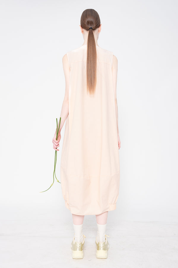 Person wearing a light pink sleeveless dress holding a flower on a white background