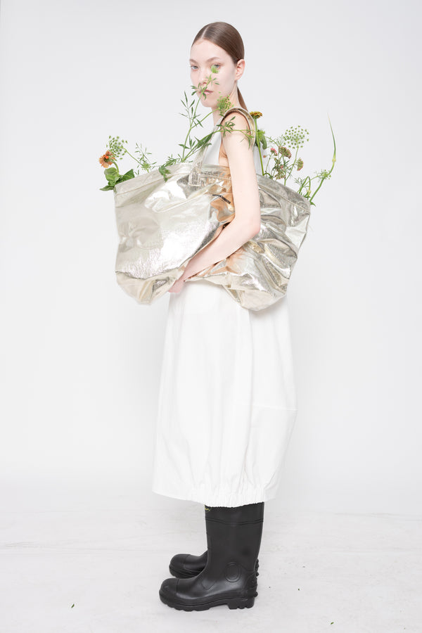 Person holding a bouquet of flowers wearing a reflective silver dress and black boots on a white background