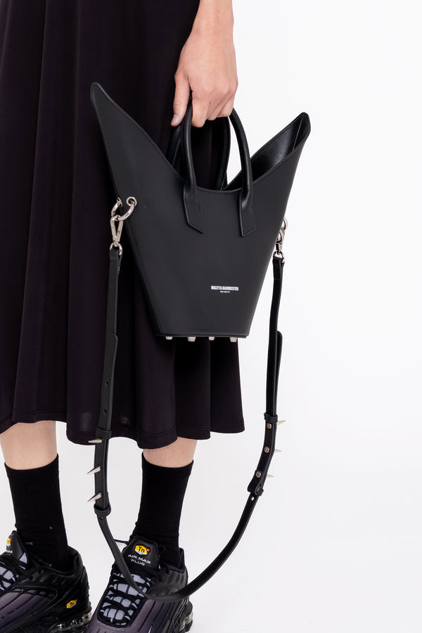 PERSON-WEARING-BLACK-DRESS-AND-ATHLETIC-SNEAKERS-AND-HOLDING-BLACK-POINTY-SHOULDER-BAG-WITH-SPIKED-CROSSBODY-STRAP-CLOSE-UP-VIEW