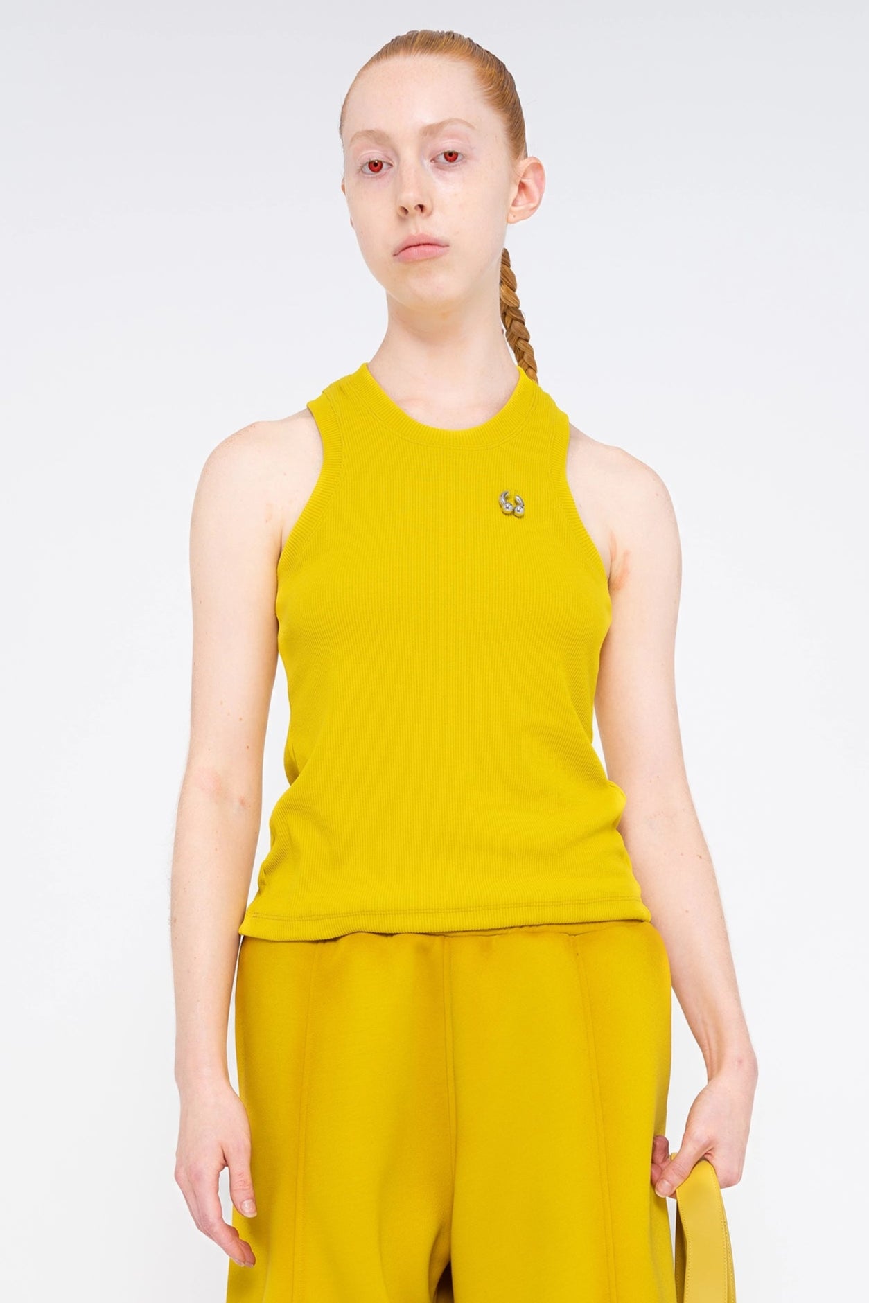 PERSON-WEARING-MUSTARD-YELLOW-TANK-WITH-PIERING-DETAIL-ON-UPPER-CHEST-NEAR-SHOULDER-WITH-MATCHING-PANTS-AND-BAG-CLOSE-UP-FRONT-VIEW