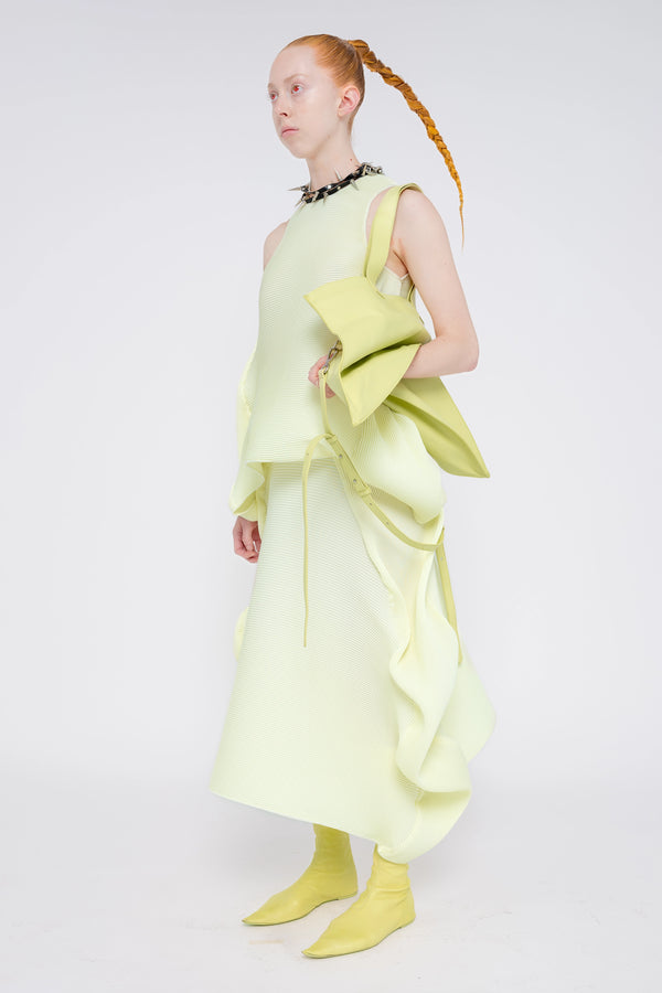 blonde-model-white-background-wearing-soft-yellow-ripple-skirt-with-matching-top-spikey-black-necklace-slouchy-soft-yellow-bag-and-soft-yellow-boots-quarter-turn-full-body