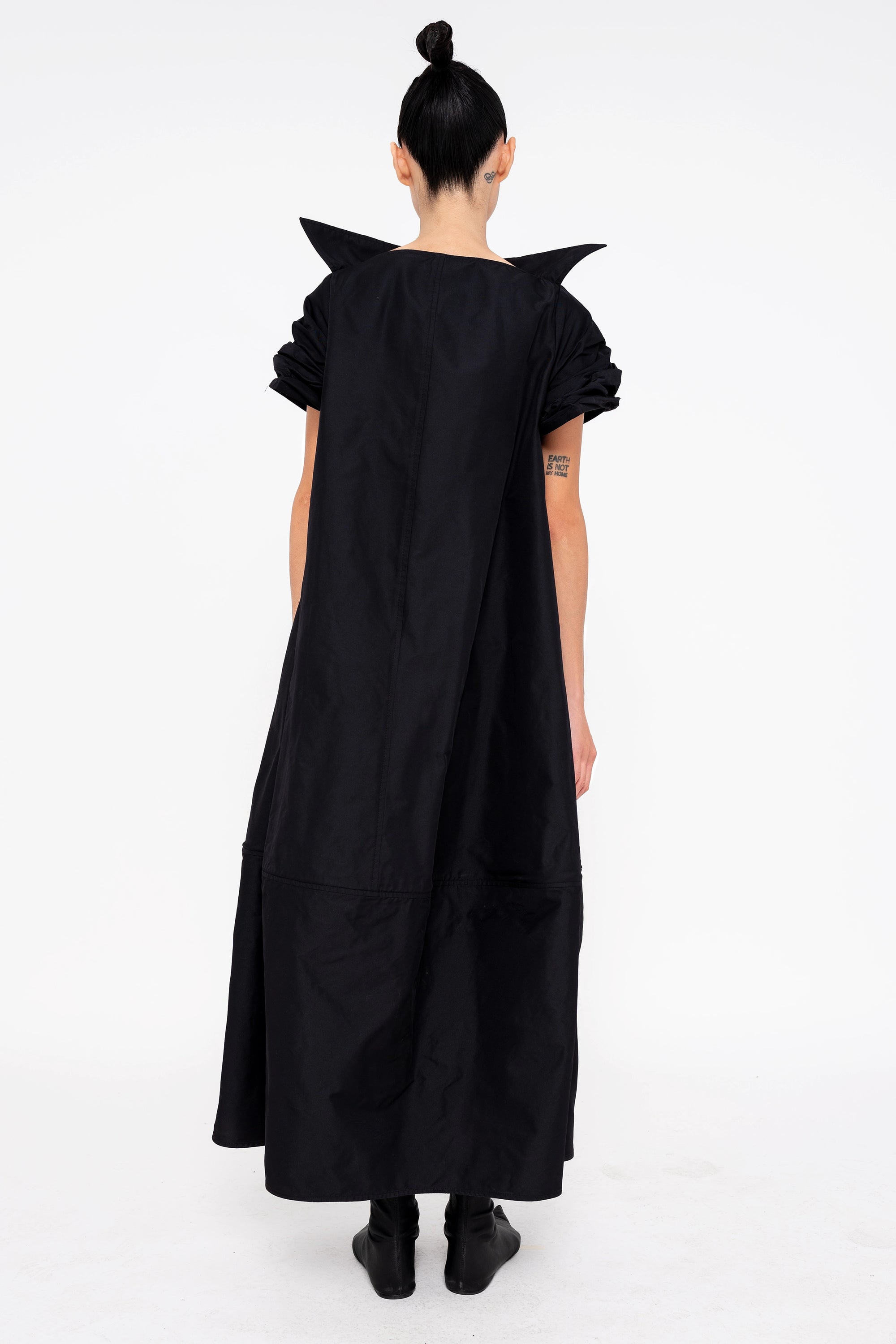 female-wearing-black-maxi-dress-with-stand-up-collar-and-short-pointy-sleeves-on-white-background-full-body-back
