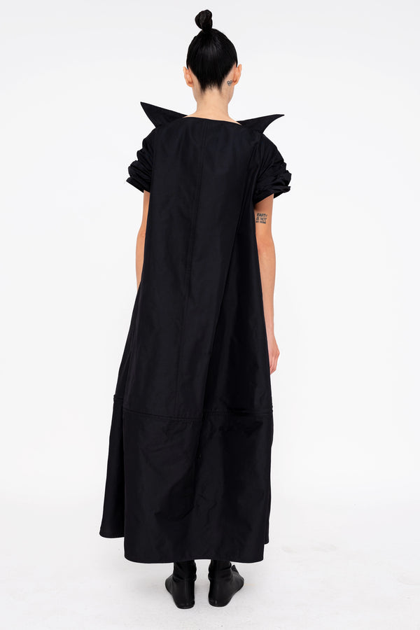 female-wearing-black-maxi-dress-with-stand-up-collar-and-short-pointy-sleeves-on-white-background-full-body-back