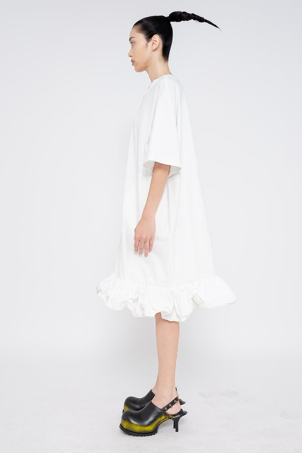 PERSON-WEARING-WHITE-TEE-DRESS-WITH-PUFFED-BOTTOM-EDGE-WITH-SPIKED-DOUBLE-HEEL-MULES-IN-PAINTED-BLACK-SIDE-VIEW