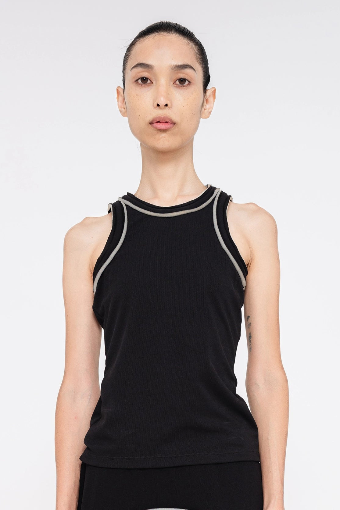 brunette-model-white-background-wearing-black-tank-top-with-foam-sleeve-and-collar-edge-detail-quarter-view-front