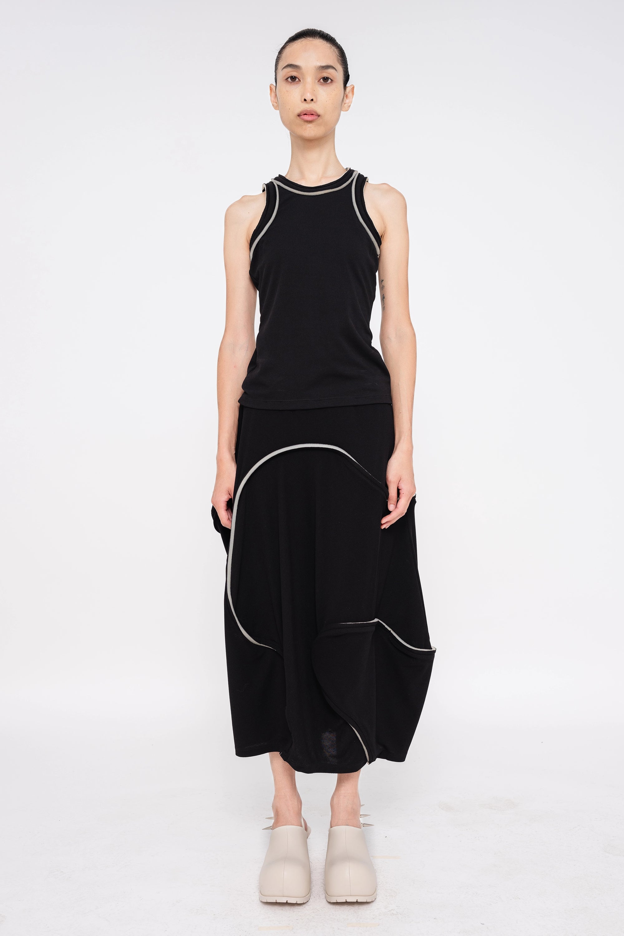 brunette-model-white-background-wearing-black-tank-top-with-foam-sleeve-and-collar-edge-detail-wearing-soft-skirt-with-foam-detail-with-off-white-double-heeled-spikey-mules-full-body-front