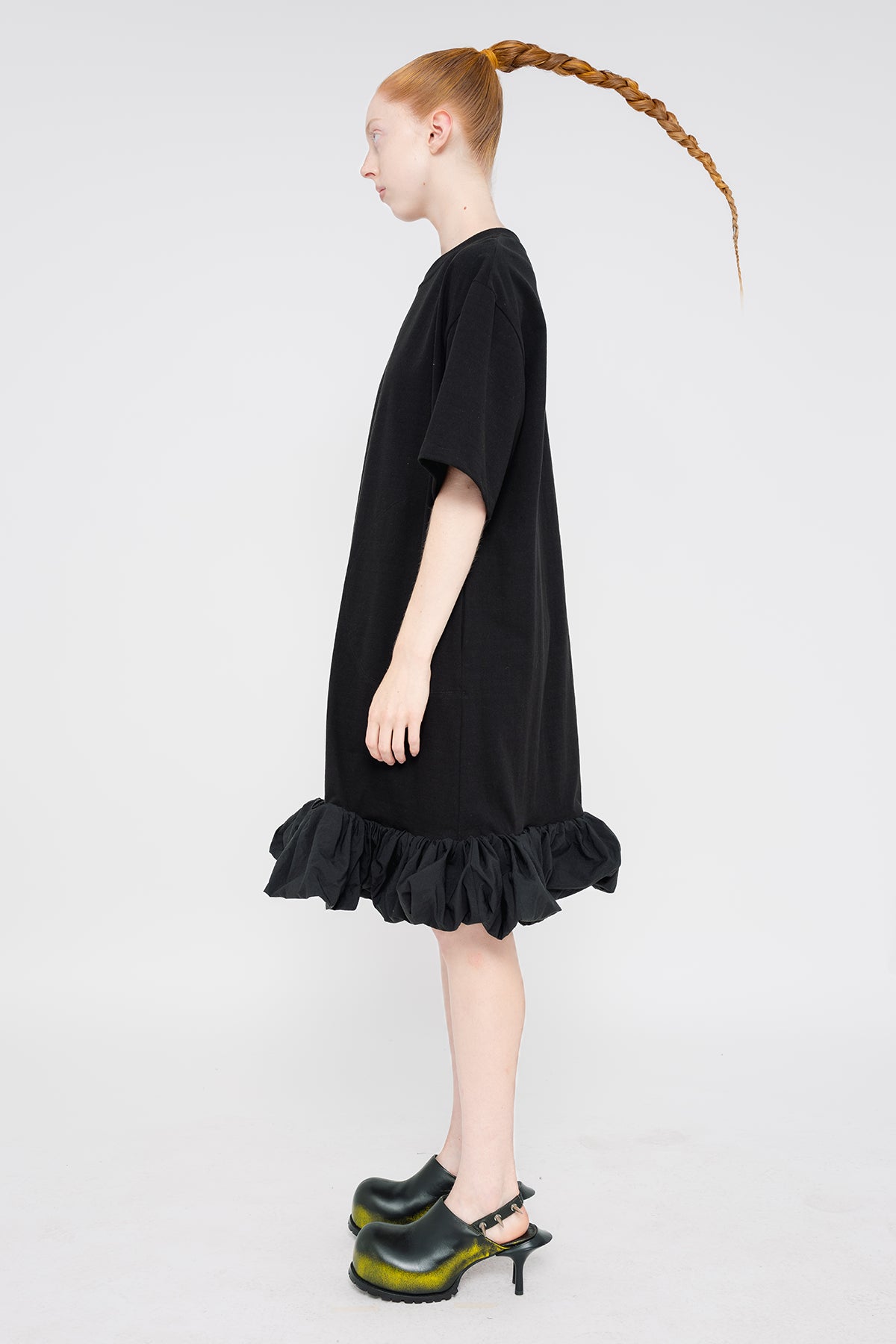 PERSON-WEARING-BLACK-TEE-DRESS-WITH-PUFFED-BOTTOM-EDGE-WITH-SPIKED-DOUBLE-HEEL-MULES-IN-PAINTED-BLACK-SIDE-VIEW