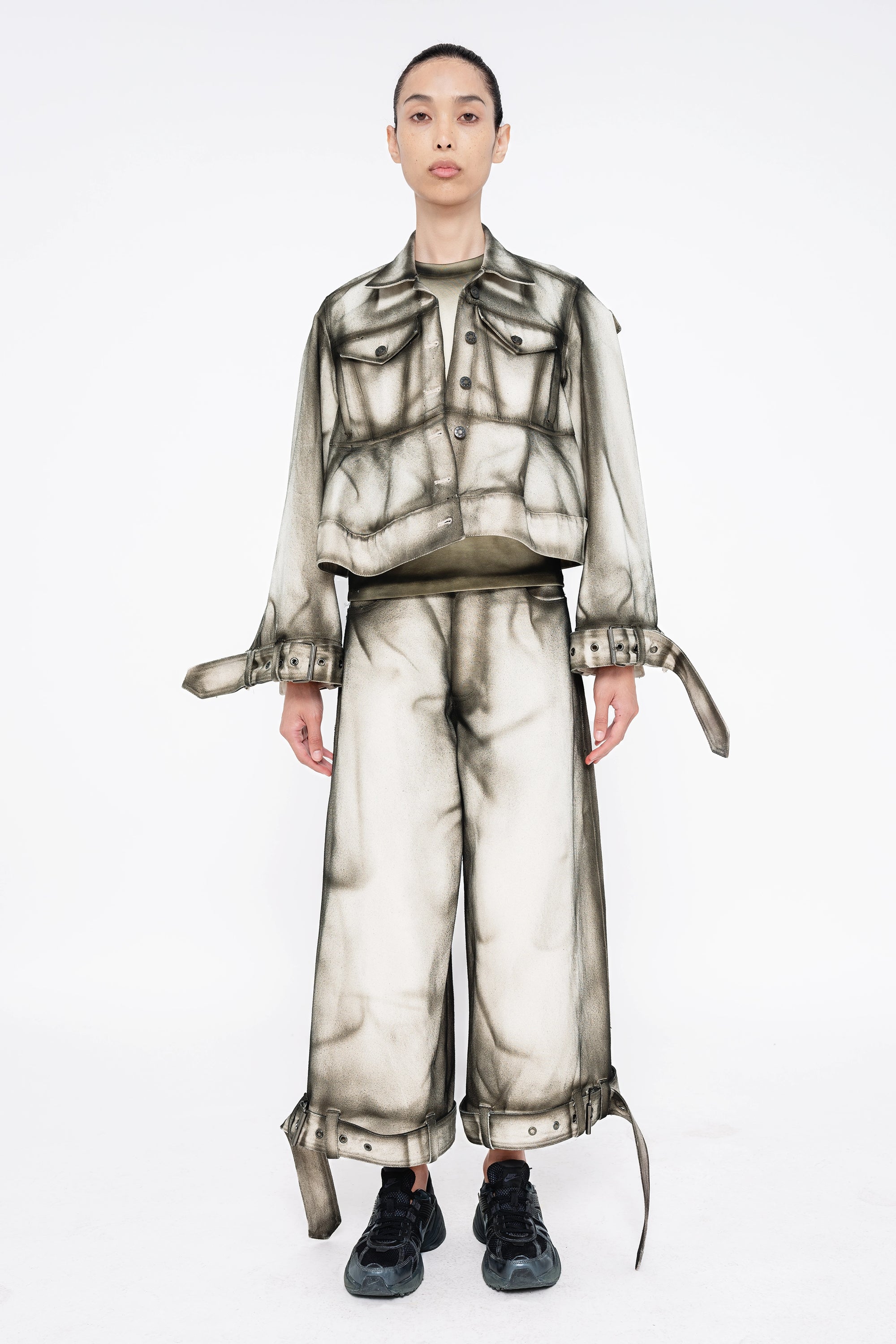 female-wearing-white-cropped-denim-jacket-and-white-cropped-denim-pants-with-black-spray-paint-at-the-seams-on-white-background-full-body-front