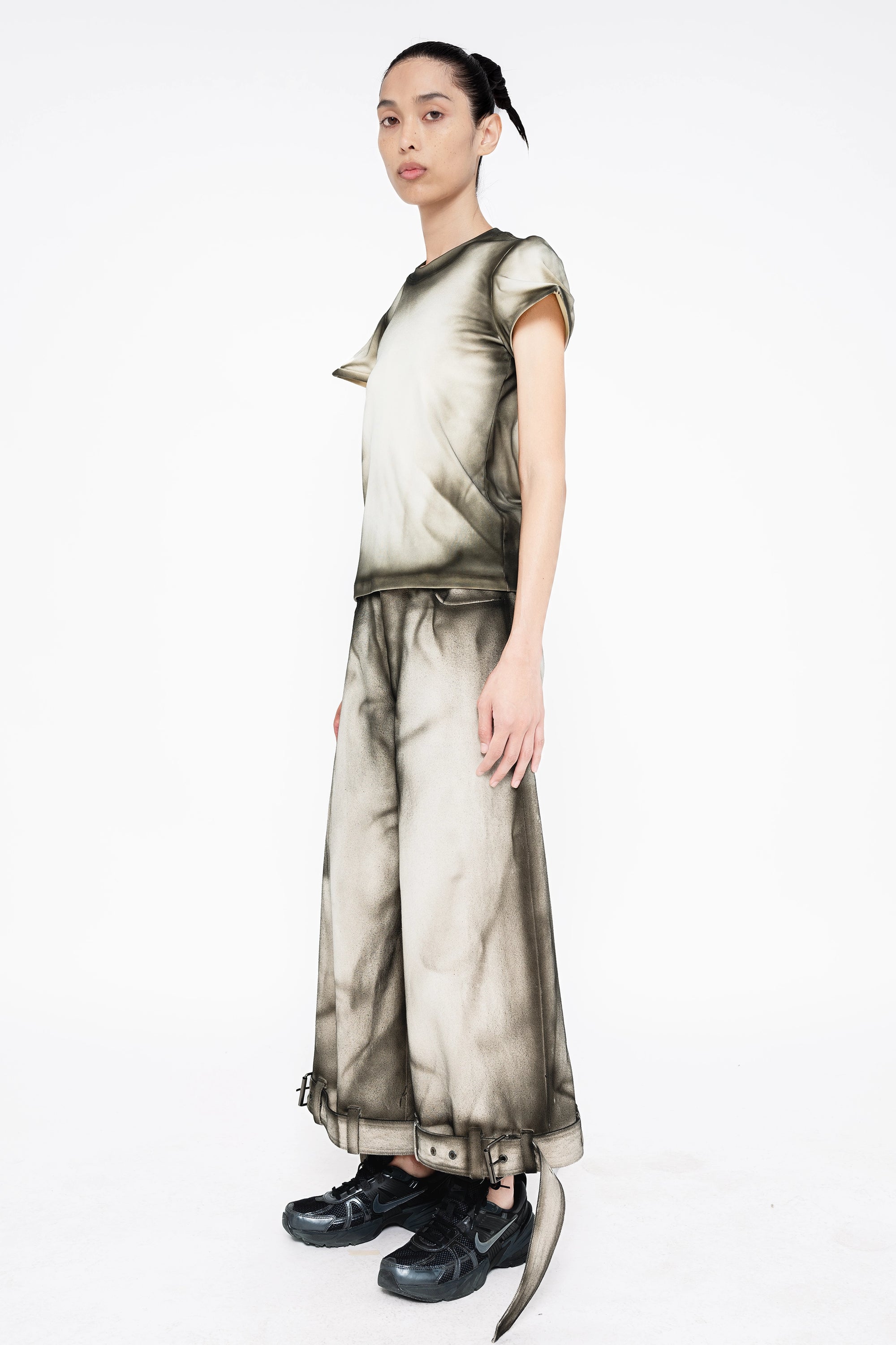 female-wearing-white-baby-tee-and-white-denim-pants-with-black-spray-paint-details-onwhite-background-full-body-three-quarter