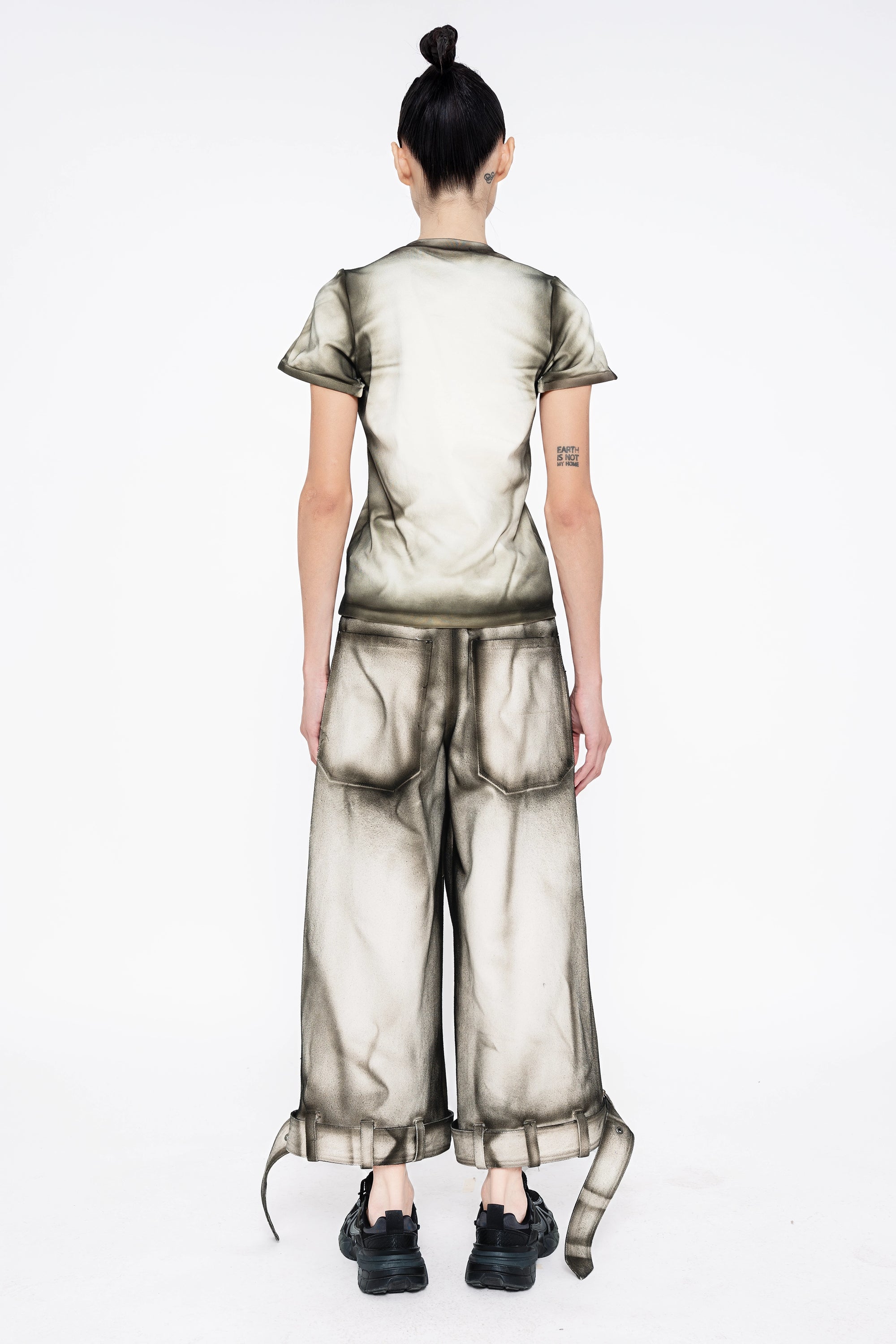female-wearing-white-baby-tee-and-white-denim-pants-with-black-spray-paint-details-onwhite-background-full-body-back