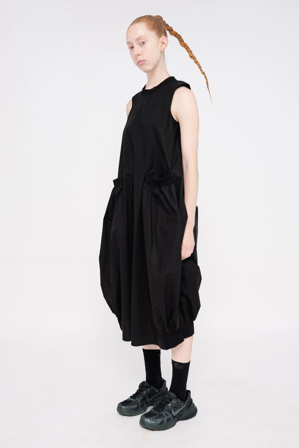 PERSON-WEARING-BLACK-SLEEVELESS-O-LINE-DRESS-WITH-FRONT-POCKETS-WITH-ATHLETIC-SNEAKERS-THREE-QUARTER-VIEW