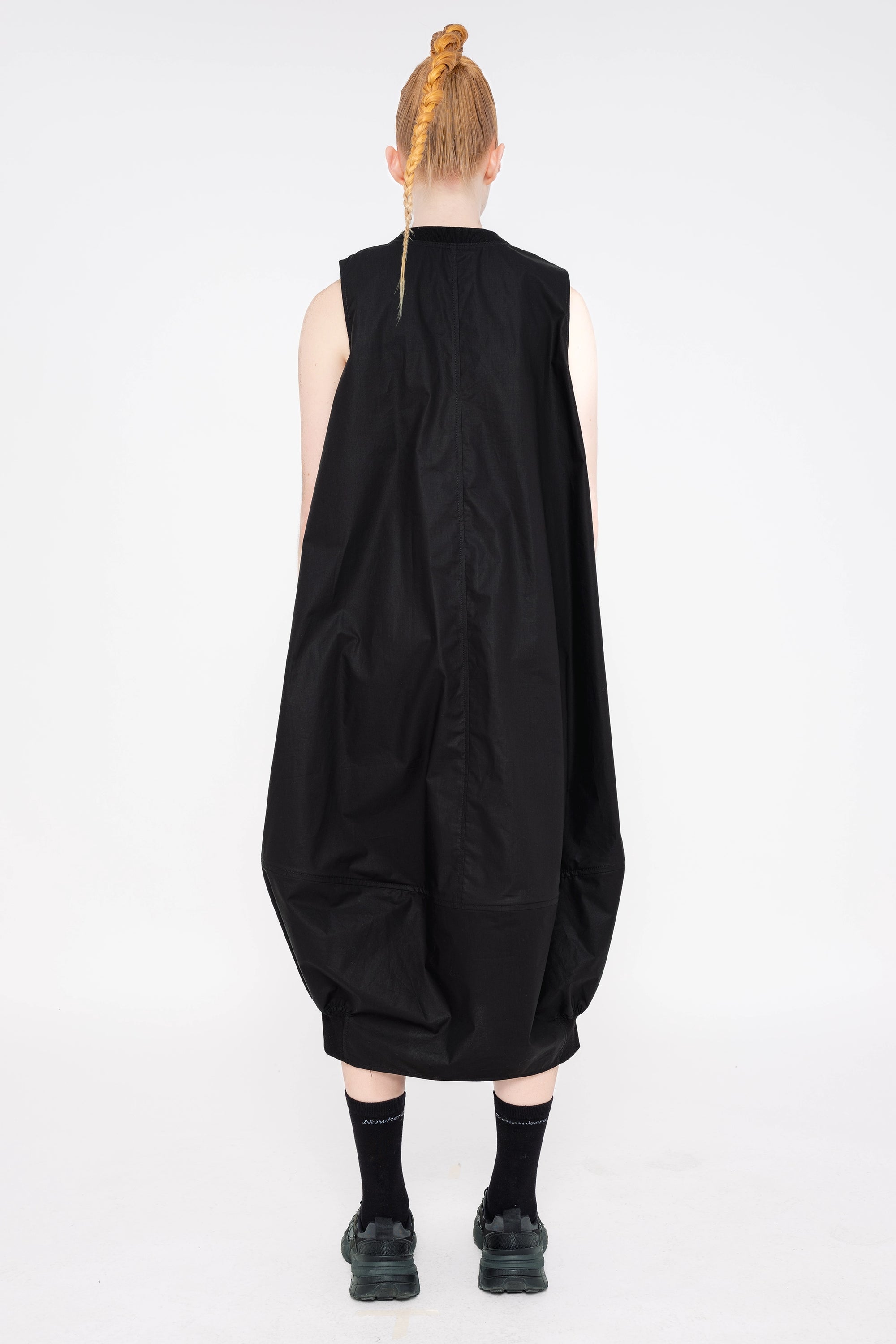 PERSON-WEARING-BLACK-SLEEVELESS-O-LINE-DRESS-WITH-FRONT-POCKETS-WITH-ATHLETIC-SNEAKERS-BACK-VIEW