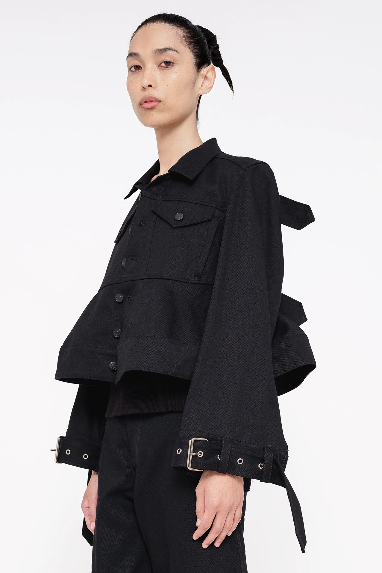 brunette-model-wearing-black-cropped-jean-jacket-with-buttons-chest-pockets-and-belted-sleeve-design-quarter-view-quarter-turn