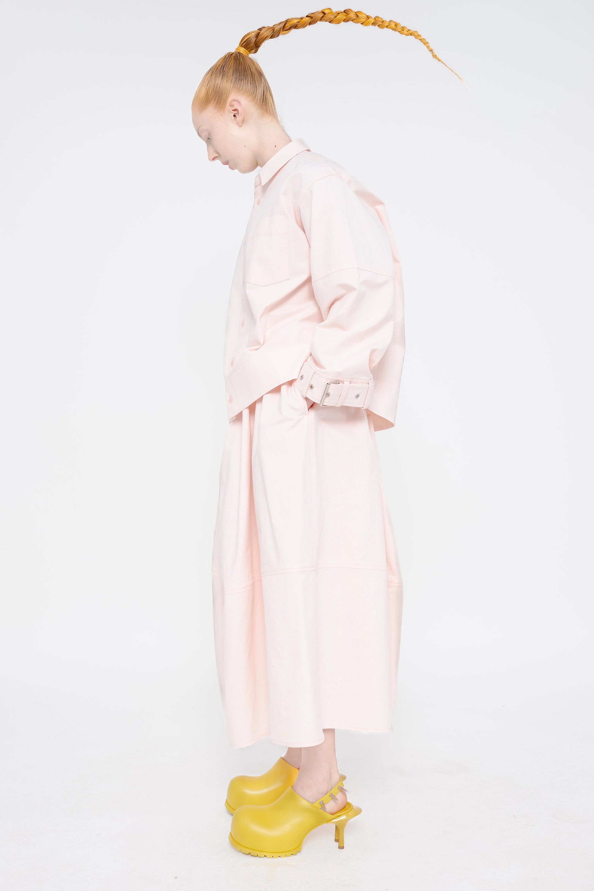 blonde-model-white-background-wearing-soft-pick-shirt-with-belted-sleeve-detail-and-soft-pink-volume-skirt-with-mustard-yellow-spikey-doubled-heeled-mules-full-body-side