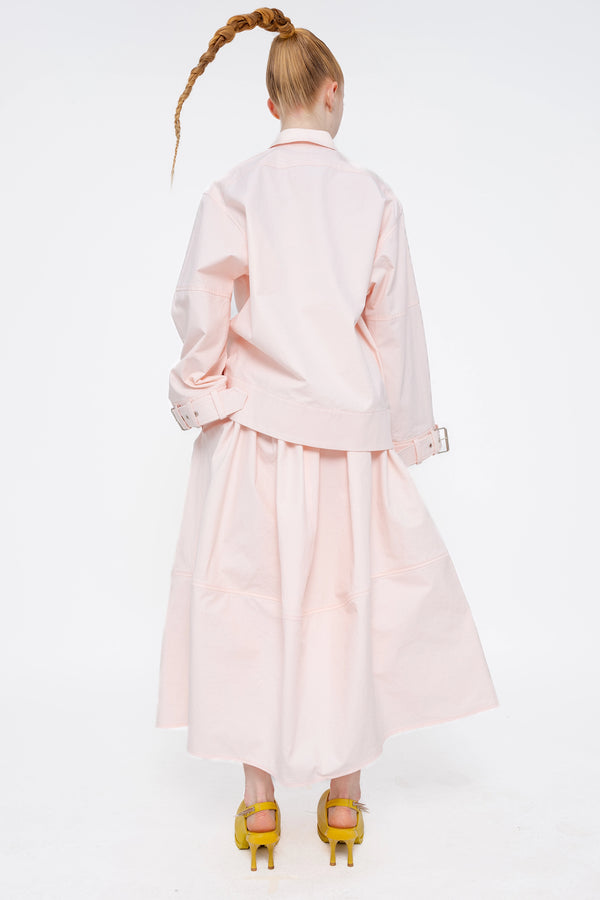 blonde-model-white-background-wearing-soft-pick-shirt-with-belted-sleeve-detail-and-soft-pink-volume-skirt-with-mustard-yellow-spikey-doubled-heeled-mules-full-body-back