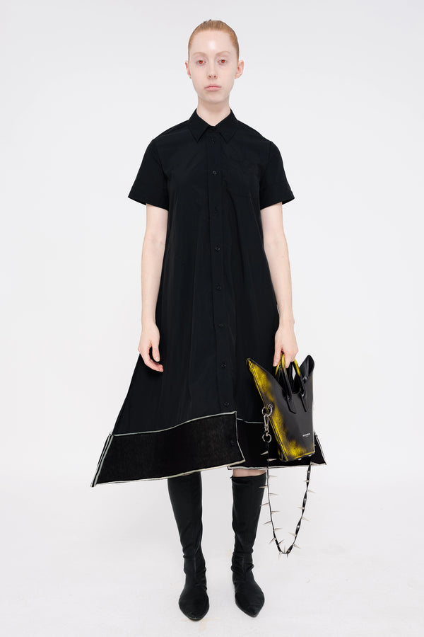 PERSON-WEARING-BLACK-A-LINE-SHORT-SLEEVE-BUTTON-DOWN-DRESS-WITH-FOAM-HEM-DETAIL-WITH-BLACK-FLAT-POINTY-TOE-BOOTS-HOLDING-PAINTED-BLACK-POINTY-SHOULDER-BAG-WITH-SPIKED-LEATHER-STRAP-FRONT-VIEW