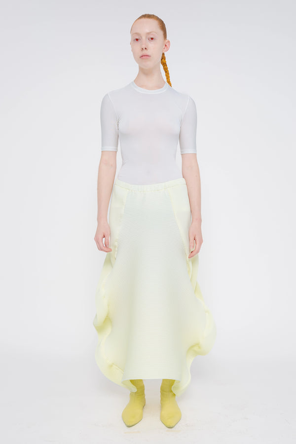 blonde-model-white-background-wearing-white-tight-top-sleeve-to-elbow-with-soft-yellow-ripple-skirt-and-soft-yellow-boots-full-body-front