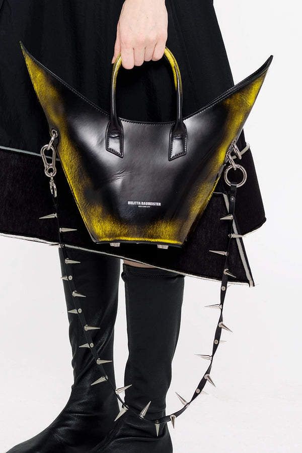 PERSON-WEARING-BLACK-DRESS-WITH-BLACK-BOOTS-HOLDING-BLACK-PAINTED-POINTY-SHOULDER-BAG-WITH-SPIKED-CROSSBODY-STRAP-CLOSE-UP