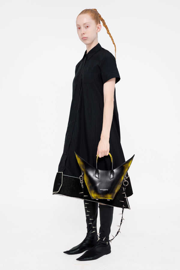 PERSON-WEARING-BLACK-A-LINE-SHORT-SLEEVE-BUTTON-DOWN-DRESS-WITH-FOAM-HEM-DETAIL-WITH-BLACK-FLAT-POINTY-TOE-BOOTS-HOLDING-PAINTED-BLACK-POINTY-SHOULDER-BAG-WITH-SPIKED-LEATHER-STRAP-THREE-QUARTER-VIEW