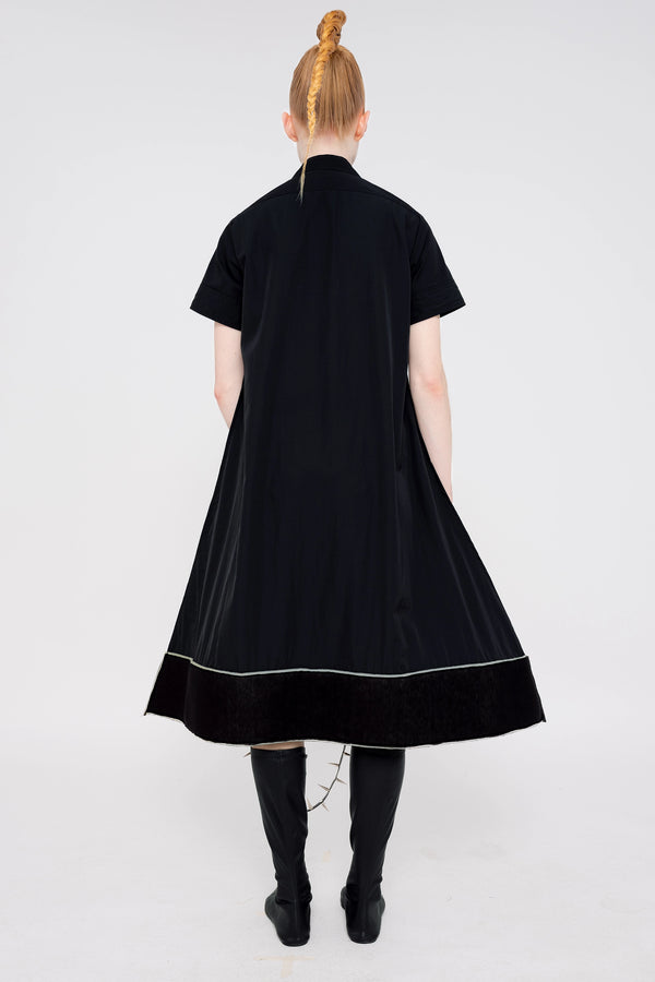 PERSON-WEARING-BLACK-A-LINE-SHORT-SLEEVE-BUTTON-DOWN-DRESS-WITH-FOAM-HEM-DETAIL-WITH-BLACK-FLAT-POINTY-TOE-BOOTS-HOLDING-PAINTED-BLACK-POINTY-SHOULDER-BAG-WITH-SPIKED-LEATHER-STRAP-BACK-VIEW