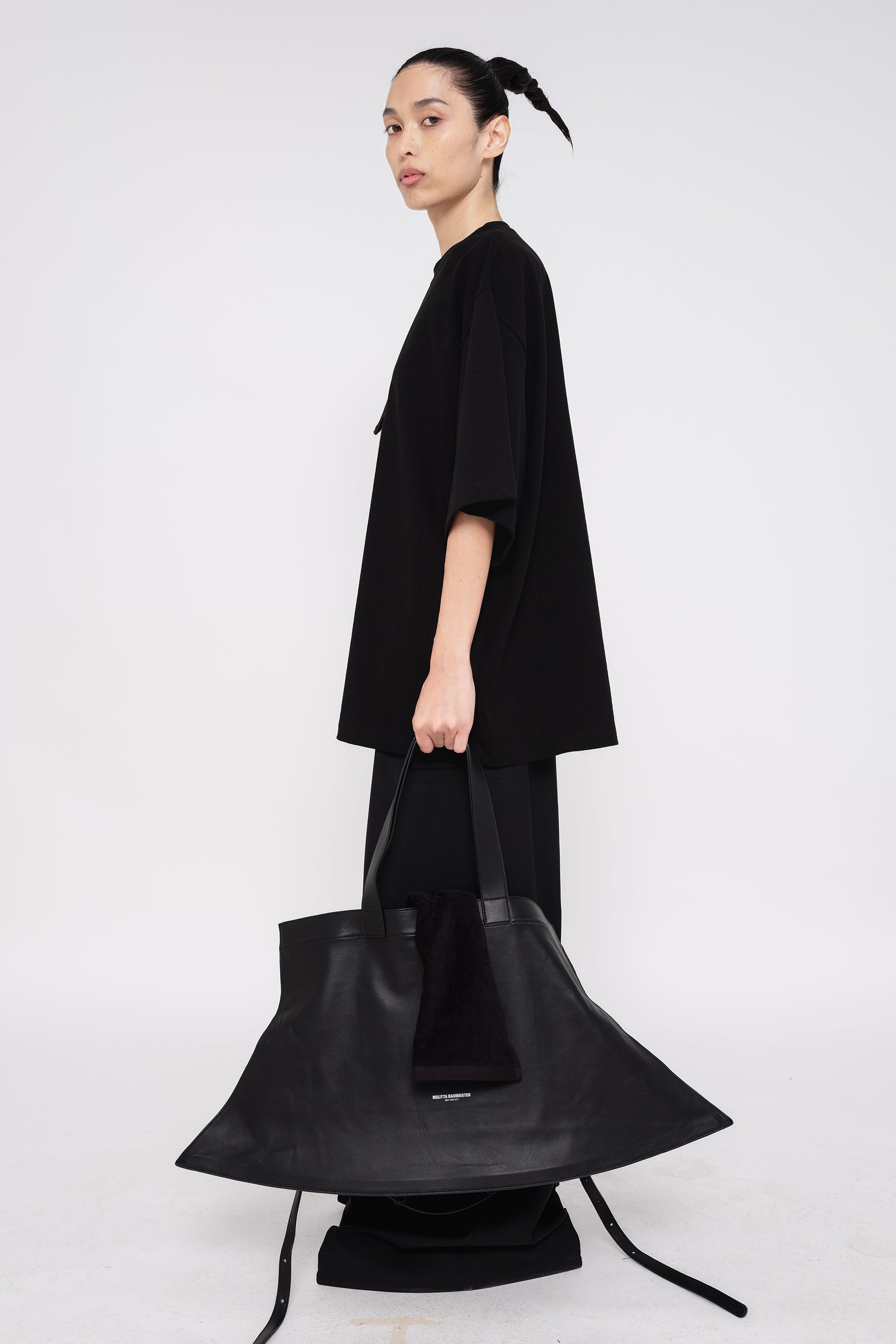 PERSON-WEARING-BLACK-SHIRT-WITH-BLACK-PANTS-AND-BLACK-SLOUCHY-POINTY-WEEKENDER-BAG-WITH-CROSSBODY-STRAP-SIDE-VIEW