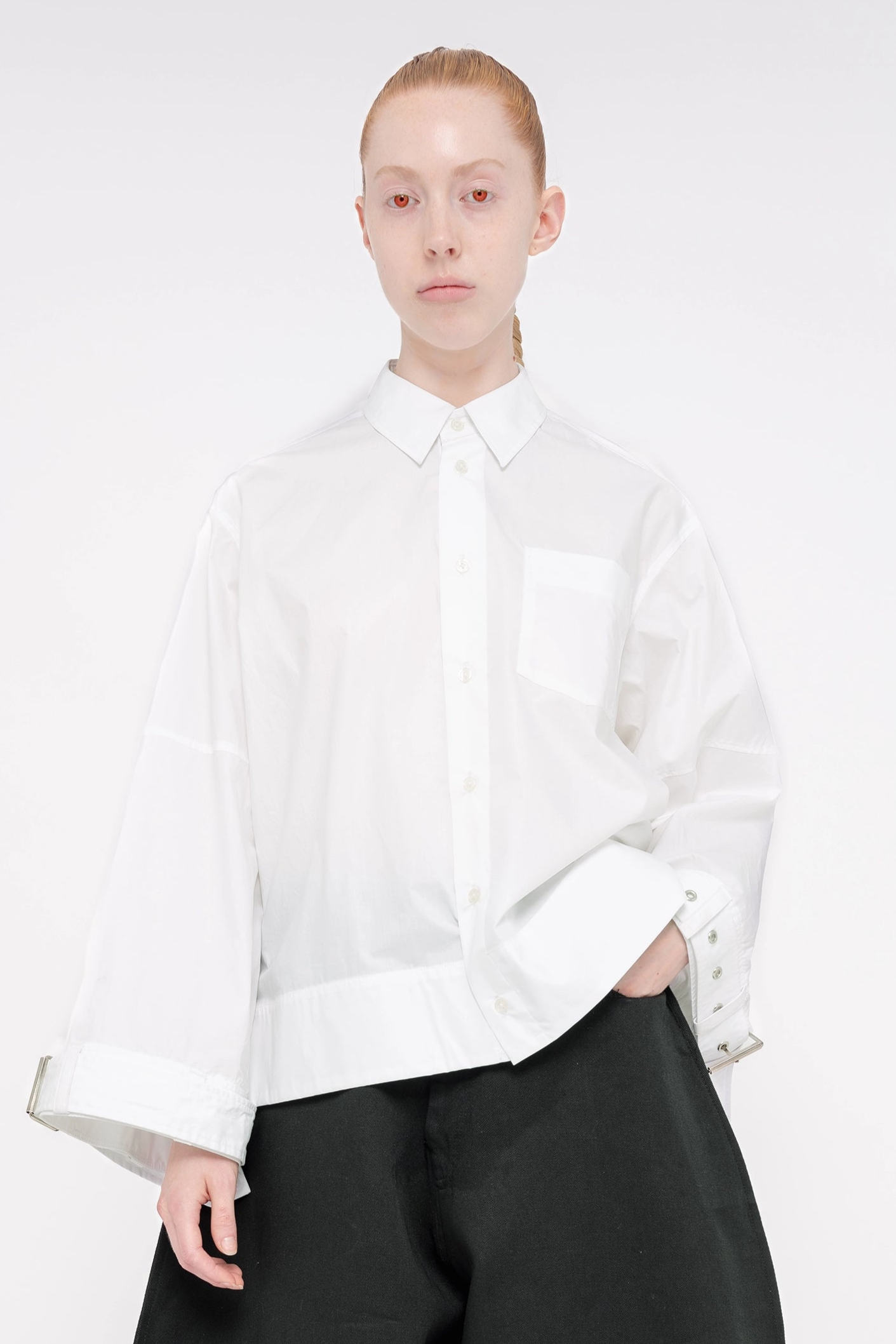 PERSON-WEARING-WHITE-BOXY-COLLARED-BUTTON-DOWN-WITH-BELTED-DETAIL-ON-SLEEVE-HEMS-WITH-BLACK-PANTS-CLOSE-UP-FRONT-VIEW