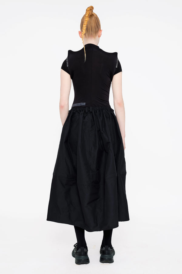 female-wearing-black-top-with-prominent-shoulders-and-white-0-screenprint-with-black-maxi-skirt-on-white-background-full-body-back