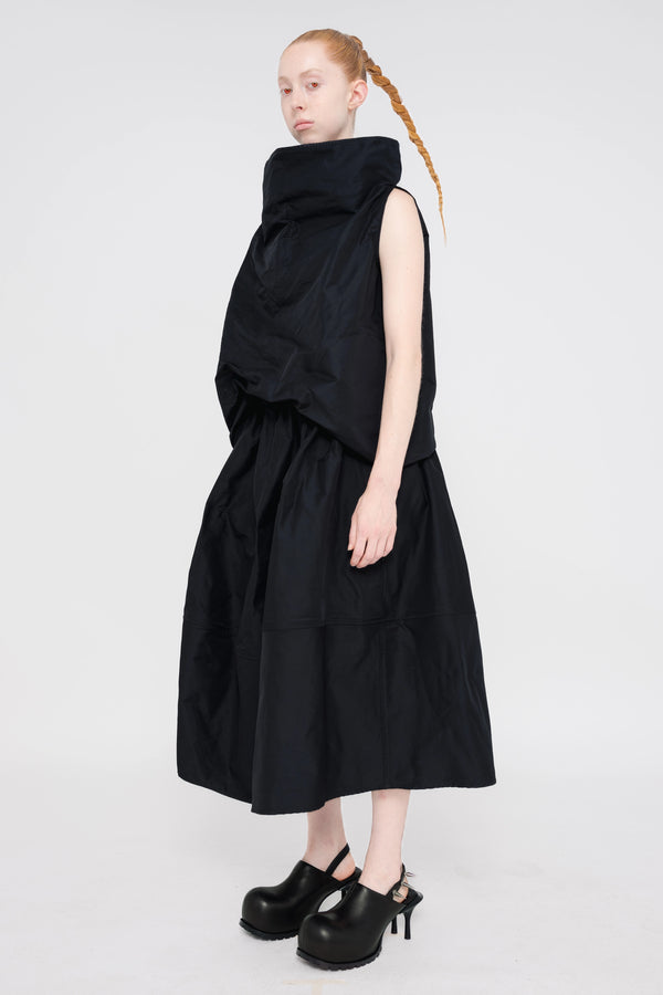 blonde-female-model-white-background-black-sleeveless-boatneck-top-and-skirt-red-eyes-and-black-spikey-doubled-heeled-mules-full-body-quarter-turn