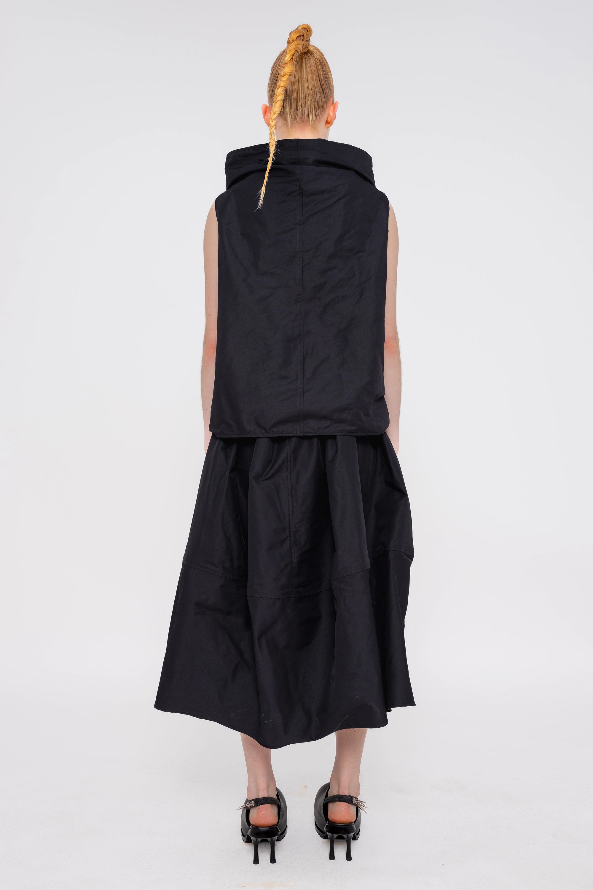 blonde-female-model-white-background-black-sleeveless-boatneck-top-and-skirt-and-black-spikey-doubled-heeled-mules-full-body-back