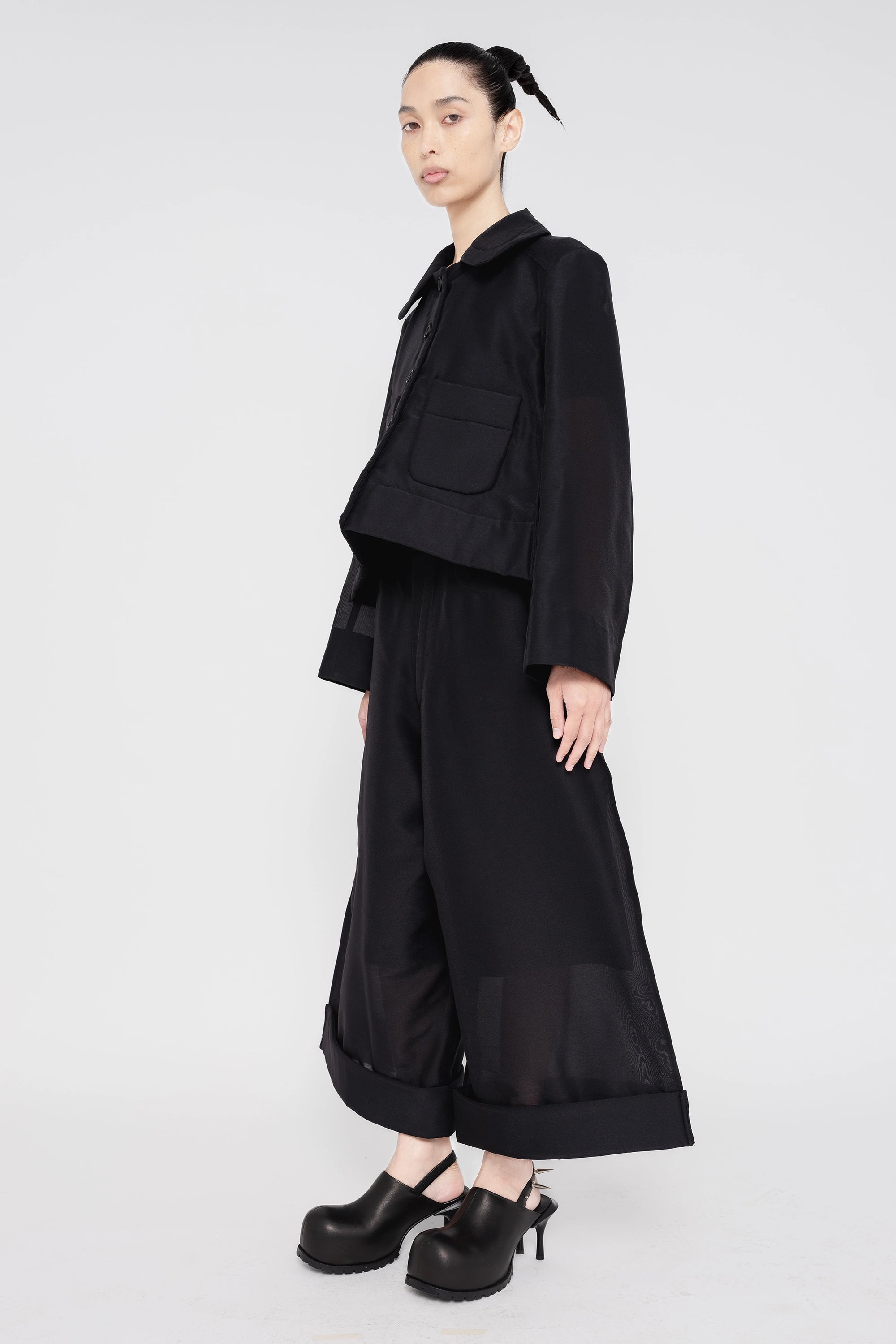 PERSON-WEARING-BLACK-A-LINE-SHIRT-JACKET-AND-MATCHING-PANTS-WITH-BLACK-SPIKED-DOUBLE-HEEL-MULES-SIDE-VIEW