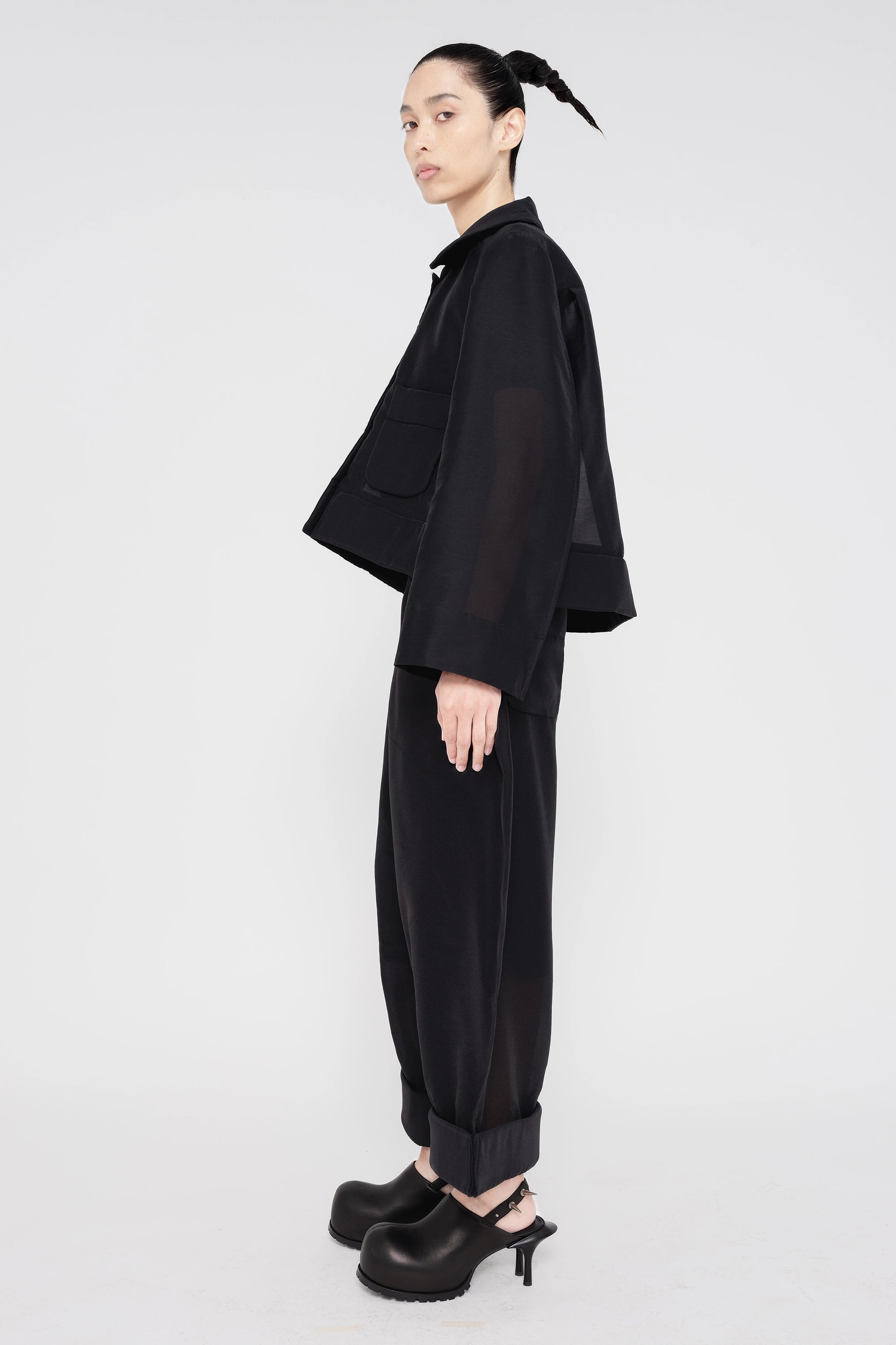 PERSON-WEARING-BLACK-A-LINE-SHIRT-JACKET-AND-MATCHING-PANTS-WITH-BLACK-SPIKED-DOUBLE-HEEL-MULES-SIDE-VIEW