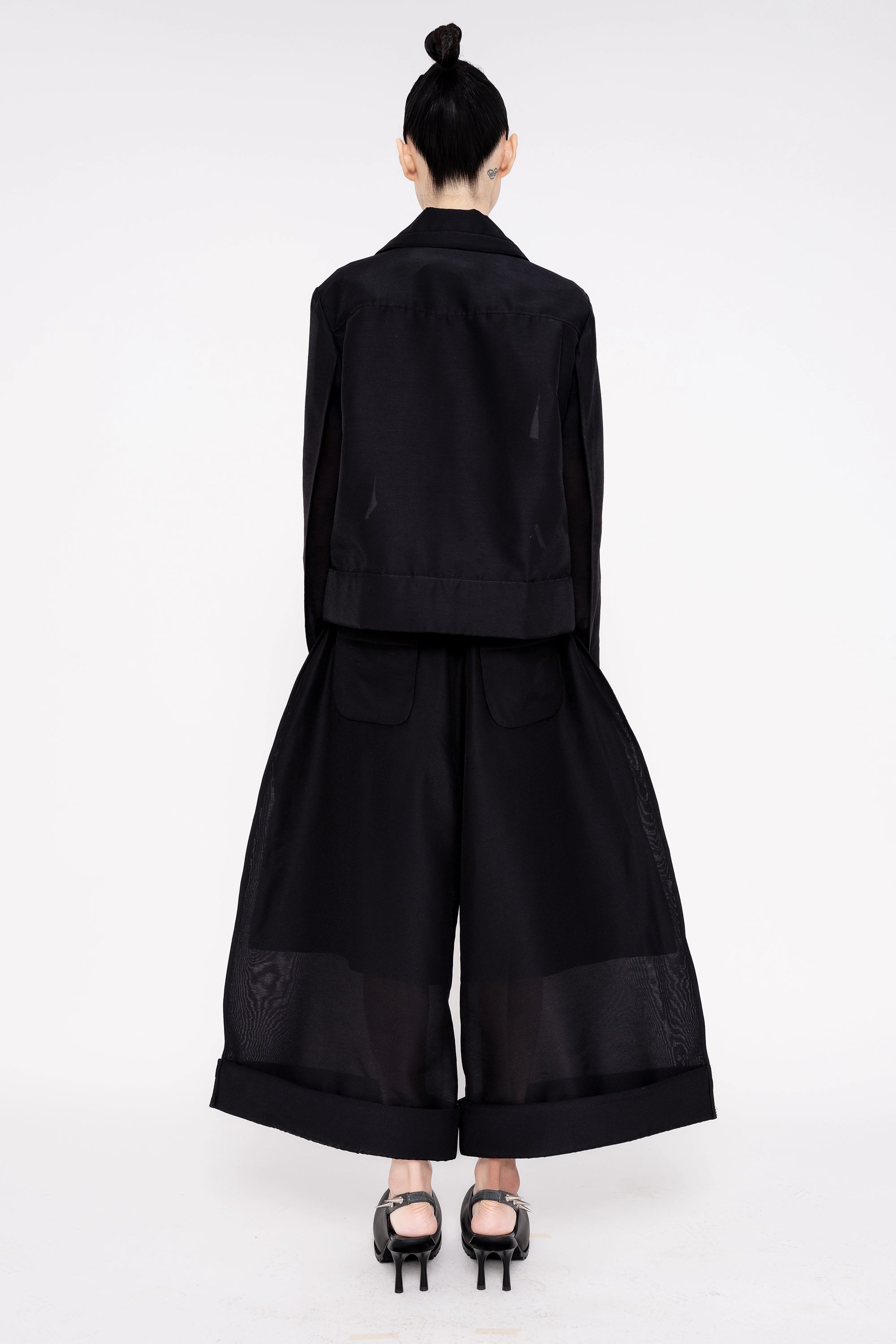 PERSON-WEARING-BLACK-A-LINE-SHIRT-JACKET-AND-MATCHING-PANTS-WITH-BLACK-SPIKED-DOUBLE-HEEL-MULES-BACK-VIEW