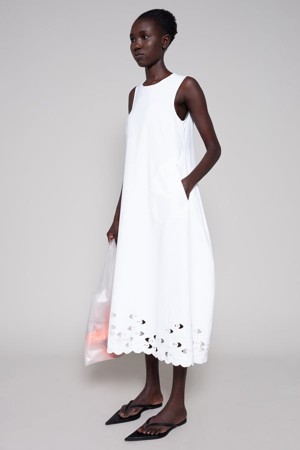 Person wearing white sleeveless dress with a tote bag on plain background