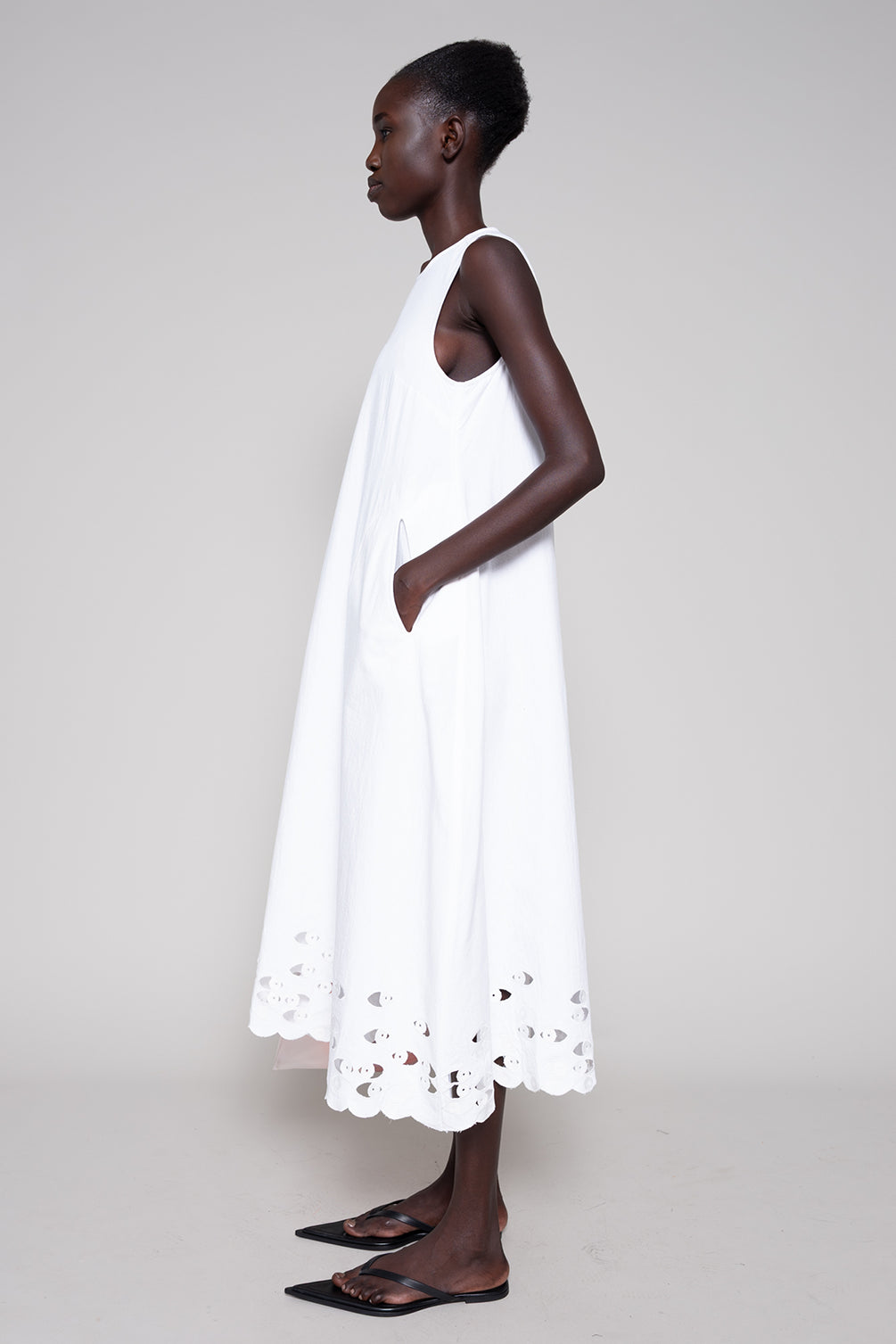 Woman wearing a white dress with cut-out details on a plain background